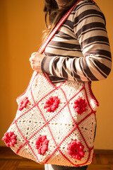 Young woman posing with a crocheted tote bag, with red flowers