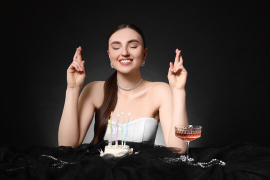 Fashionable photo of attractive young woman making wish with her Birthday cake on black background