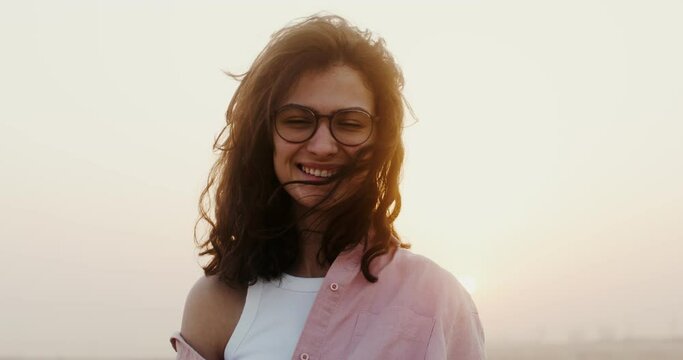 A young beautiful woman of European appearance in glasses with curly short hair smiles while looking at the camera standing in the desert