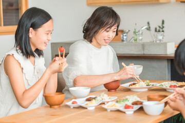 家のダイニングテーブルで朝食を食べる親子・家族・ファミリー（母親と子供・中学生・小学生）

