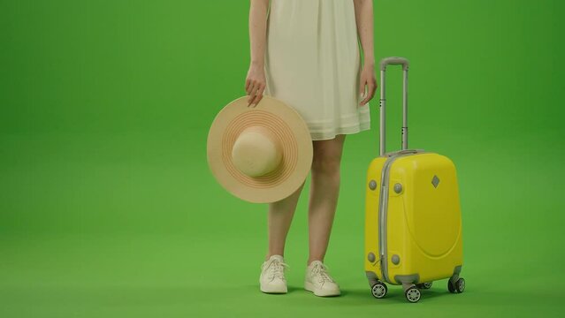 Green Screen. Chroma Key. Woman Legs in White Shoes and White Dress Carrying her Yellow Travel Luggage on the Wheels and Hat in the Hands