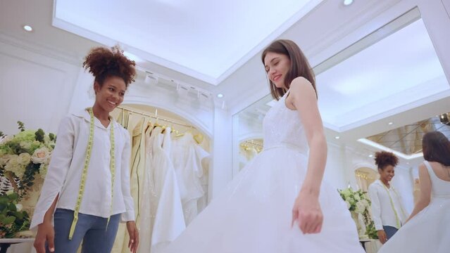 Beautiful bride trying the wedding dress with helper female in studio.
