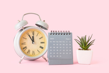 Flip paper calendar for August with alarm clock and houseplant on pink background