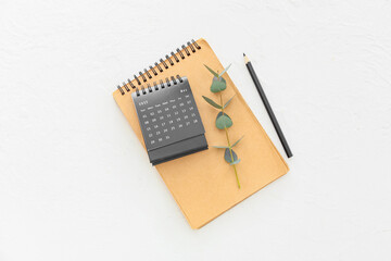 Flip paper calendar with notebook and eucalyptus branch on light background