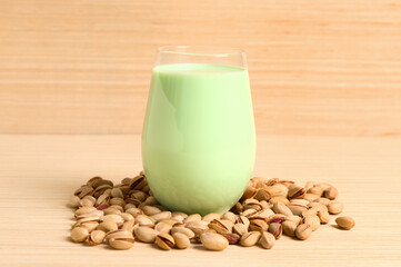 Glass of healthy pistachio milk and nuts on table near wooden table