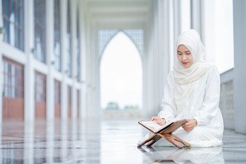 Obraz premium The image of an Asian Muslim woman in the Islamic religion in hijab in white color. reading the Quran and having a happy smiling face Staying in a beautiful mosque out of respect for God.