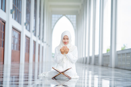 The image of an Asian Muslim woman in the Islamic religion in hijab in white color. reading the Quran and having a happy smiling face Staying in a beautiful mosque out of respect for God.