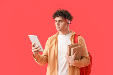 Male student with tablet computer and books on red background