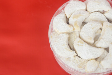 Kue putri salju or princess snow cookies. Is melt in the mouth cookies has a shape of crescent coated in icing sugar and popular indonesian cookies for Eid Mubarak. In red background.