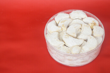 Kue putri salju or princess snow cookies. Is melt in the mouth cookies has a shape of crescent coated in icing sugar and popular indonesian cookies for Eid Mubarak. In red background.