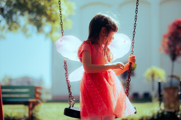 Little Girl Wearing Fairy Wings Playing in a Swing at the Playground. Happy child plays outdoors like in a fairytale 
