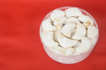 Kue putri salju or princess snow cookies. Is melt in the mouth cookies has a shape of crescent coated in icing sugar and popular indonesian cookies for Eid Mubarak. In red background.