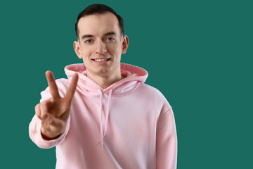 Young man showing two fingers on green background, closeup
