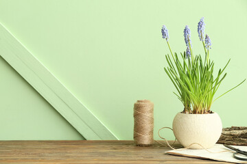 Vase with beautiful Muscari flowers on wooden table near green wall