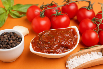 Bowl of delicious tomato sauce and ingredients on orange background, closeup