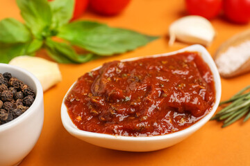 Bowl of delicious tomato sauce and ingredients on orange background, closeup