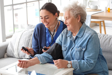 Young caregiver measuring blood pressure of senior woman at home