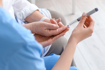 Young caregiver measuring sugar level of senior woman in bedroom, closeup