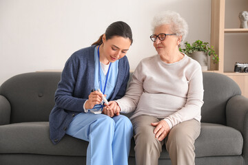 Young caregiver measuring sugar level of senior woman at home