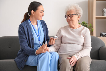 Young caregiver measuring sugar level of senior woman at home