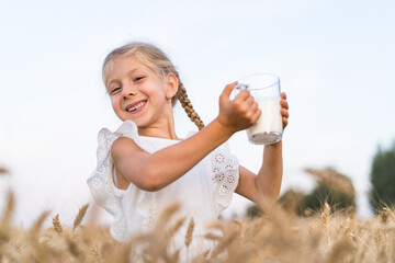 little blonde girl with pigtails in a rye field with a mug of milk, the concept of healthy eating,...