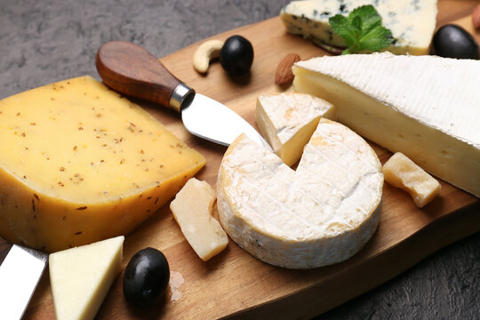 Wooden board with different types of tasty cheese on dark background, closeup