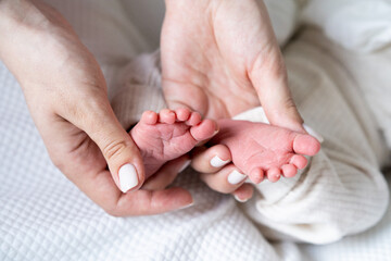 baby legs in the hands of the mother, photo on a light background, the feet of the newborn in...