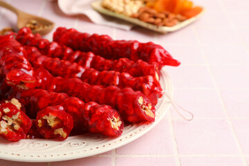 Plate with tasty churchkhela on pink tile background, closeup