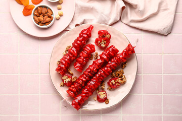 Plate with tasty churchkhela on pink tile background