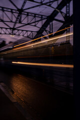 Naklejka premium Defocused Lights of cars at night in Krakow bridge. Street line lights. Night highway city. Long exposure photograph night road. Colored bands of red light trails on the road. Background wallpaper