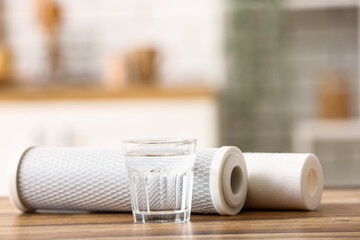 Glass of water with filters on wooden table in kitchen
