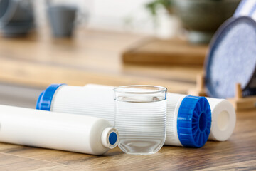 Glass of water with filters on wooden table in kitchen