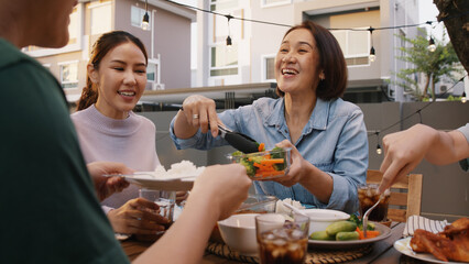 Mom enjoy thai meal cooking for family day home dining at dine table cozy patio. Mum passing serving food to group four asia people young adult man woman friend fun joy relax warm night picnic eating.