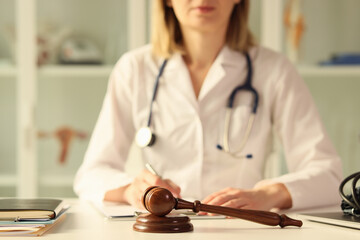 Wooden judge gavel on table female doctor doing paperwork on background
