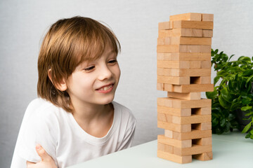 happy boy playing board game, building a tower of wooden cubes, logic game for child development