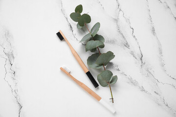 Bamboo toothbrushes and eucalyptus branch on white marble background