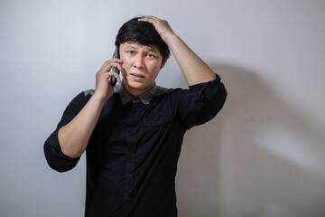 A mature Asian man in a black shirt holds a cell phone with an expression of surprise and disapproval