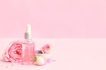 Bottle of cosmetic oil with rose extract and flowers on pink background