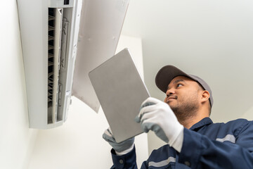 Technician in uniform using tablet to check list of maintenance and cleaning filters of air conditioner. Air condition maintenance service. Home services concept.