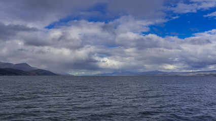 Ripples on the blue water of the Beagle Canal. In the distance, against the background of the azure sky and clouds - a mountain range. Argentina. Tierra del Fuego Archipelago.