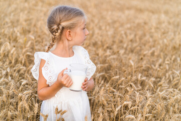 Fototapeta na wymiar little blonde girl with pigtails in a rye field with a mug of milk, the concept of healthy eating, eco friendly farm products