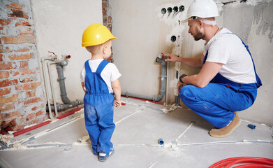 Man and kid working together on home renovation. Father and child in safety construction helmet...