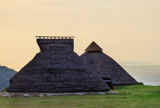 Historic thatched roof huts on grassy coastal hill in Jomon village