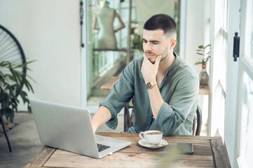 handsome young businessman Working on laptop and working online while sitting at coffee shop table, businessman working outdoors side view
