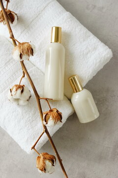 Cosmetic skincare bottles mockup, white towels and cotton flowers top view on gray background with copy space. Product presentation. Beauty and body care products. Neutral beige colors. 