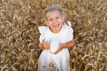 little blonde girl with pigtails in a rye field with a mug of milk, the concept of healthy eating, eco friendly farm products