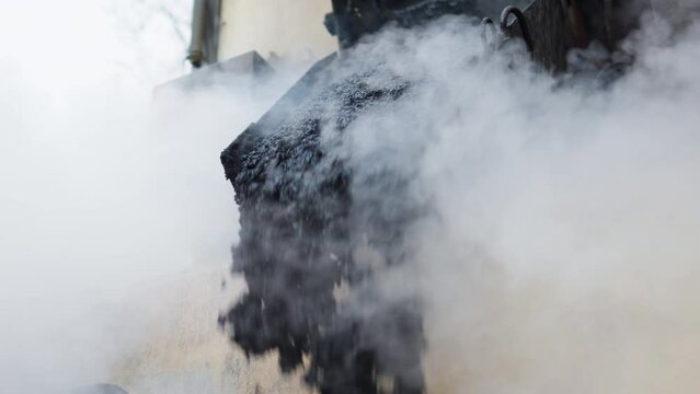 Heavy paver machinery dropping fresh hot black asphalt bitumen on the ground with smoke - low angle