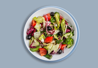 Delicious vegetable Greek salad with feta in a plate on a blue isolated background. Healthy diet food concept.