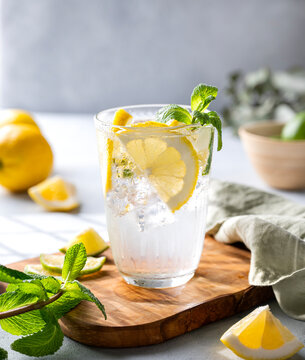 Lemonade drink with fresh lemons, lime, mint and ice. Refreshing citrus mojito cocktail on a light background with shadow. Summer cold drinks concept.
