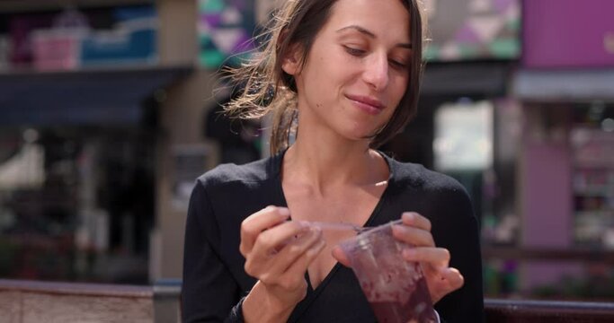 Woman in 20s sits outside resturant and eats Acai treat - South American dessert